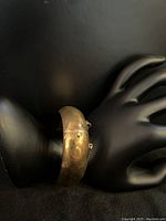 Side view of polished thick gold bangle on black display