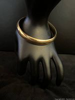Polished yellow gold bangle bracelet on display hand showing full profile