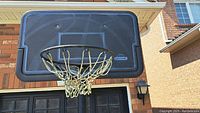 Close-up of the black backboard and netted hoop attached to a brick wall background.