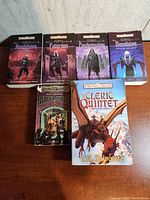 Six fantasy paperback books by R.A. Salvatore arrayed on a wooden surface, showing front covers including The Cleric Quintet and Dark Elf Trilogy titles.