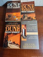 Six Dune series books by Frank Herbert arranged on wooden surface, showing front cover artwork and titles
