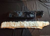 Two long faux fur strips, one black and grey, one white, laid flat on black background