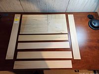 Top-down view of six basswood strips arranged neatly with one larger wooden piece with pencil markings, on a wooden surface.