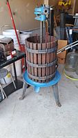 Full view of the wine juice extractor showing wooden slatted barrel, blue cast iron base and pressing mechanism.