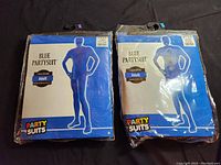 Packaged blue adult morphsuits, front packaging showing labeled sizes Large and XL, unopened.