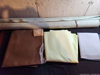Multiple rolls and sheets of pleather material in beige, off-white, brown, cream/yellow, and white colors shown side-by-side on table
