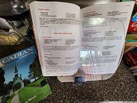 Open recipe book laid on countertop showing recipe pages; several more recipe books visible stacked beneath.