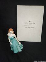Front view of Royal Doulton Zodiac Leo porcelain figurine with original box labeled 'Signs of the Zodiac'. Figurine features a young woman in a teal dress.