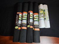 Six rolls of non-adhesive shelf liners: 4 black with textured bubbles sized 18" x 50" and 2 off-white with swirl pattern sized 12" x 49".