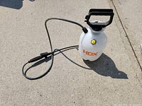 HDX brand 1-gallon multipurpose sprayer with hose and spray nozzle resting on concrete.