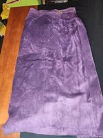Long purple suede skirt laid flat, showing gold-tone button detail at waist
