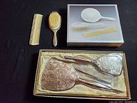Photo showing silver plated vanity set with heart-shaped mirror, brush, comb, and extra matching brush and comb, with ornate floral engraving