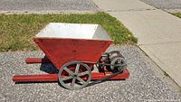 Front view of the red wooden base with large hopper, showing the feeding chute and wheels.
