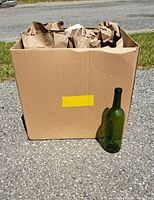 Cardboard box filled with 22 green glass wine bottles packed upright and partially wrapped with brown paper packing material.
