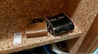 View of both binoculars in their respective cases placed on a wooden shelf, highlighting wear on the cases