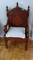 Full view of antique wooden bishop's chair showing carved arms, decorative floral inlay, and finials.