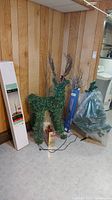 Artificial greenery reindeer figure, boxed twinkle tree, and wrapped 42-inch indoor tree on floor against wood panel wall.