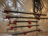 Five bar clamps of varying lengths arranged horizontally on the floor with a set of black V belts coiled nearby