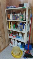 Shelf with multiple cleaning products in plastic bottles and spray cans including floor finisher, bleach, and other liquids.