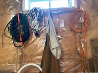 Photo showing multiple extension cords in green, black, white, and orange hanging on a plastic-covered basement wall with two aprons hung between cords.