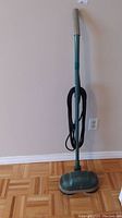 Full view of the floor polisher standing upright against wall and floor, showing handle and cord.