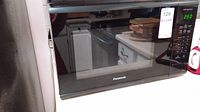 Exterior front view of black Panasonic microwave with reflective door and digital control panel showing 2:50 time.