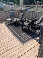 Outdoor carpet placed on a wooden deck with patio furniture partially on top. The carpet shows its size and fit on the deck area.