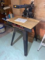Radial saw on stand in basement workshop area with manual on work surface.