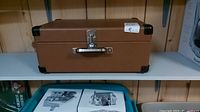 Closed brown suitcase-style record player case on a white shelf