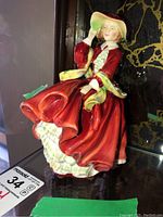 Front side view of Royal Doulton figurine featuring a woman in a red dress holding a green hat.