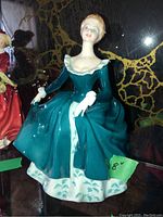 Royal Doulton figurine named Janine, model HN2461, showing full figure in teal and white dress, sitting or posed holding skirt sides.