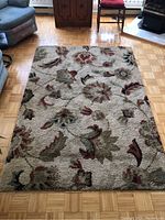 Full view of rectangular floral pattern beige rug on parquet floor, shows overall design and condition.