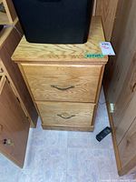 Wooden filing cabinet with two drawers and metal handles, photographed from front.