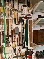 Full side view of pegboard with various woodworking and hand tools hung including saws, clamps, levels.