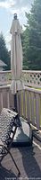 Photo showing the full closed beige cantilever umbrella with a chocolate brown frame on the deck, attached to a weighted base stand.