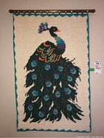 Full view of the woven wall hanging featuring a peacock design, attached to a decorative rod for display.