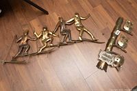 Photo showing one of the metal wall art pieces with four skiers holding ski poles on a metal rod mounted as a wall hanging, placed on a wood floor.