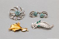 Overall photo of 3 brooches and pair of earrings, showing all items together on gray background.