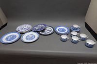 Full lot of Tuscan English teacup and saucer sets plus an assortment of Asian style blue and white china plates arranged on table.