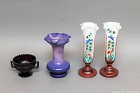 Photo shows four Victorian crystalware pieces: dark embossed bowl, purple ruffled vase, and two hand-painted milk glass tulip vases on wooden bases.