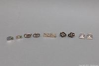 Full lot view of five pairs of sterling silver cufflinks arranged side-by-side showing shape, design, and tarnish.