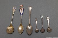 Top view of five old spoons showing enamel crests and various designs.