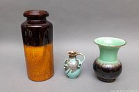 Three vintage items: tall brown-orange West German vase, small turquoise creamer with silver overlay, and green/brown flared vase.