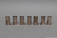 Front view of seven antique sterling silver reticulated partial lipstick cases side by side, showing intricate openwork design and overall shape.