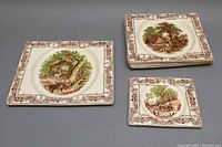 Five Royal Staffordshire rectangular plates arranged with larger plates in a stack and smaller plate adjacent, showing detailed rustic scenes and borders.