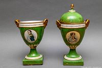 Front view of both green porcelain urns on square pedestal bases, one with lid in place