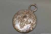 Back of the hand mirror showing detailed embossed sterling silver pattern with a monogram.