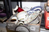 Box containing assorted plates, bowls, teapot, and other chinaware items.
