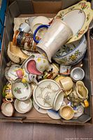 Photo showing varied chinaware including character mugs, bowls with floral patterns, saucers, and a decorative plate with gold trim.
