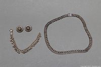 Full view of necklace, bracelet, and earrings on gray background showing overall condition and design.